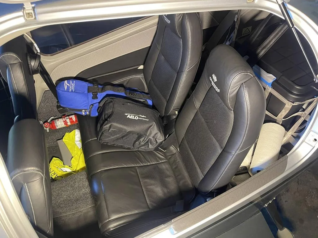 The interior cabin of a Diamond DA42 aircraft showing black leather seats and cargo area.