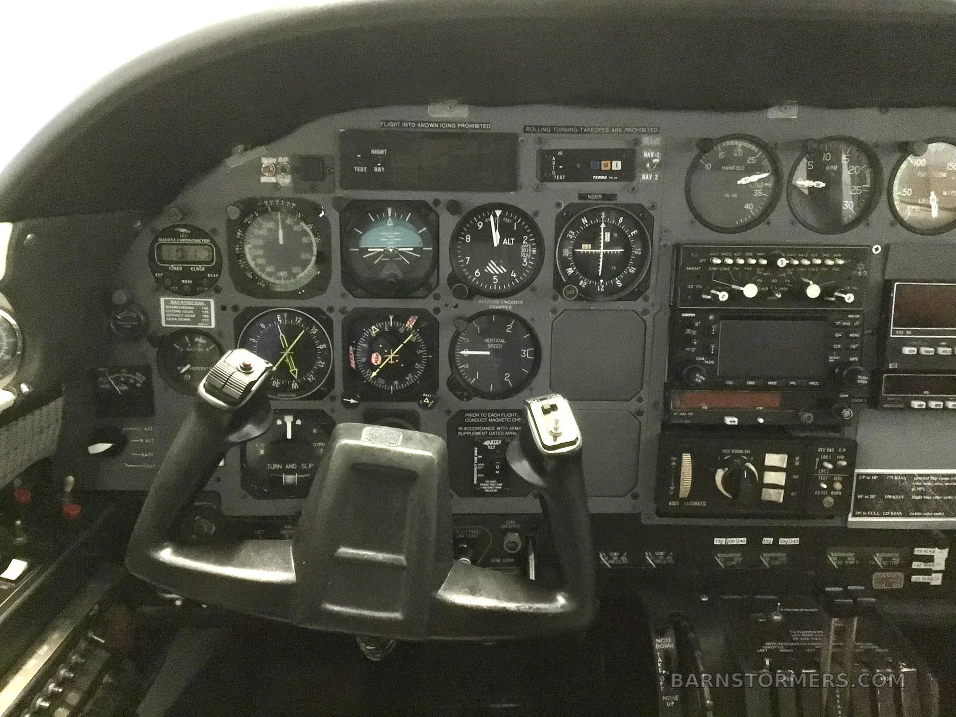 The cockpit instrument panel of an aircraft, featuring analog gauges, avionics, and two control yokes.