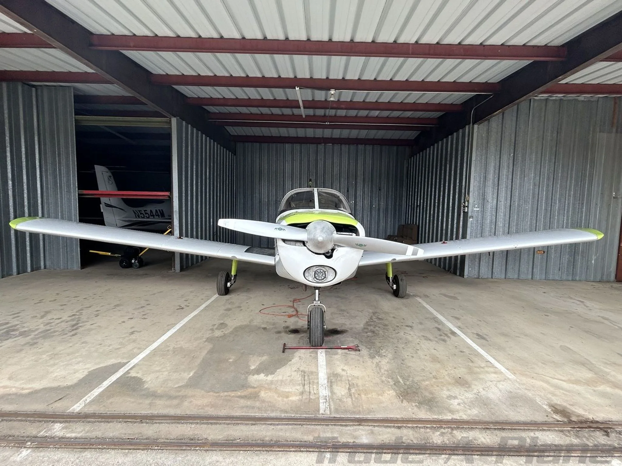 A light gray single-engine aircraft with lime green accents parked head-on in a hangar.