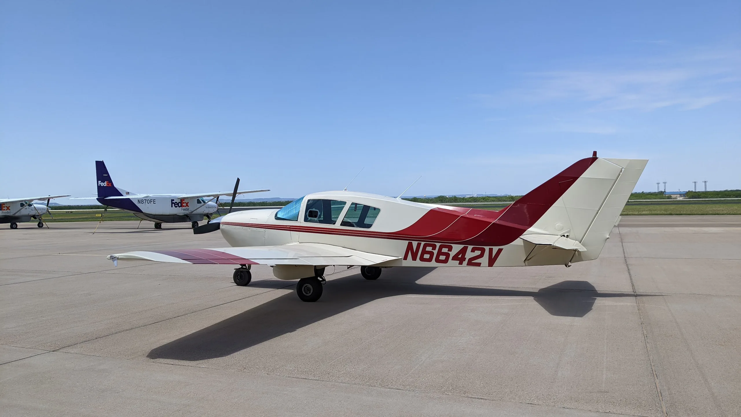 A white and red Bellanca aircraft with tail number N6642V parked on an airfield with other aircraft in the background.