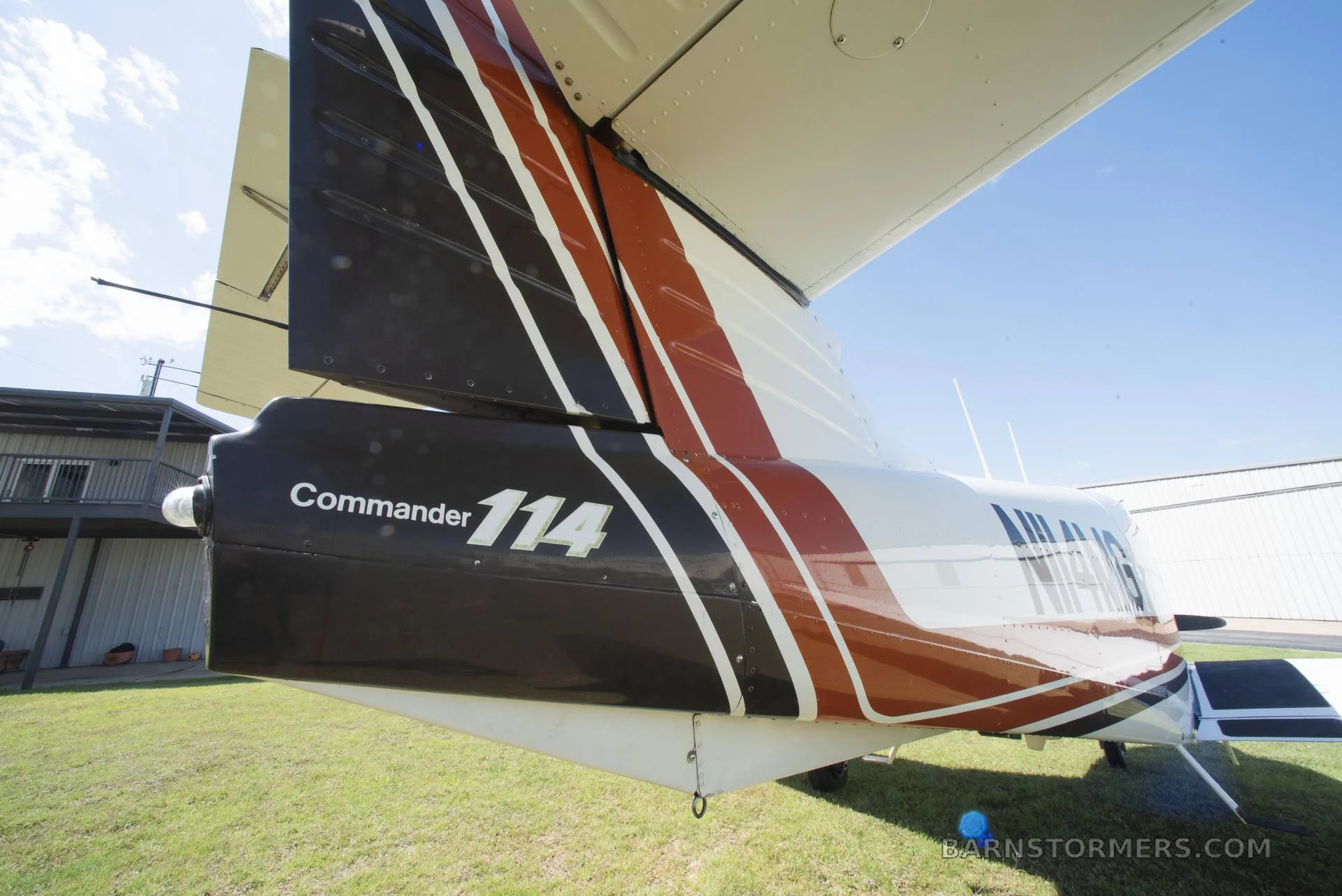 A close-up of the tail of a white, brown, and black Commander 114 aircraft, showing the registration N114MG.