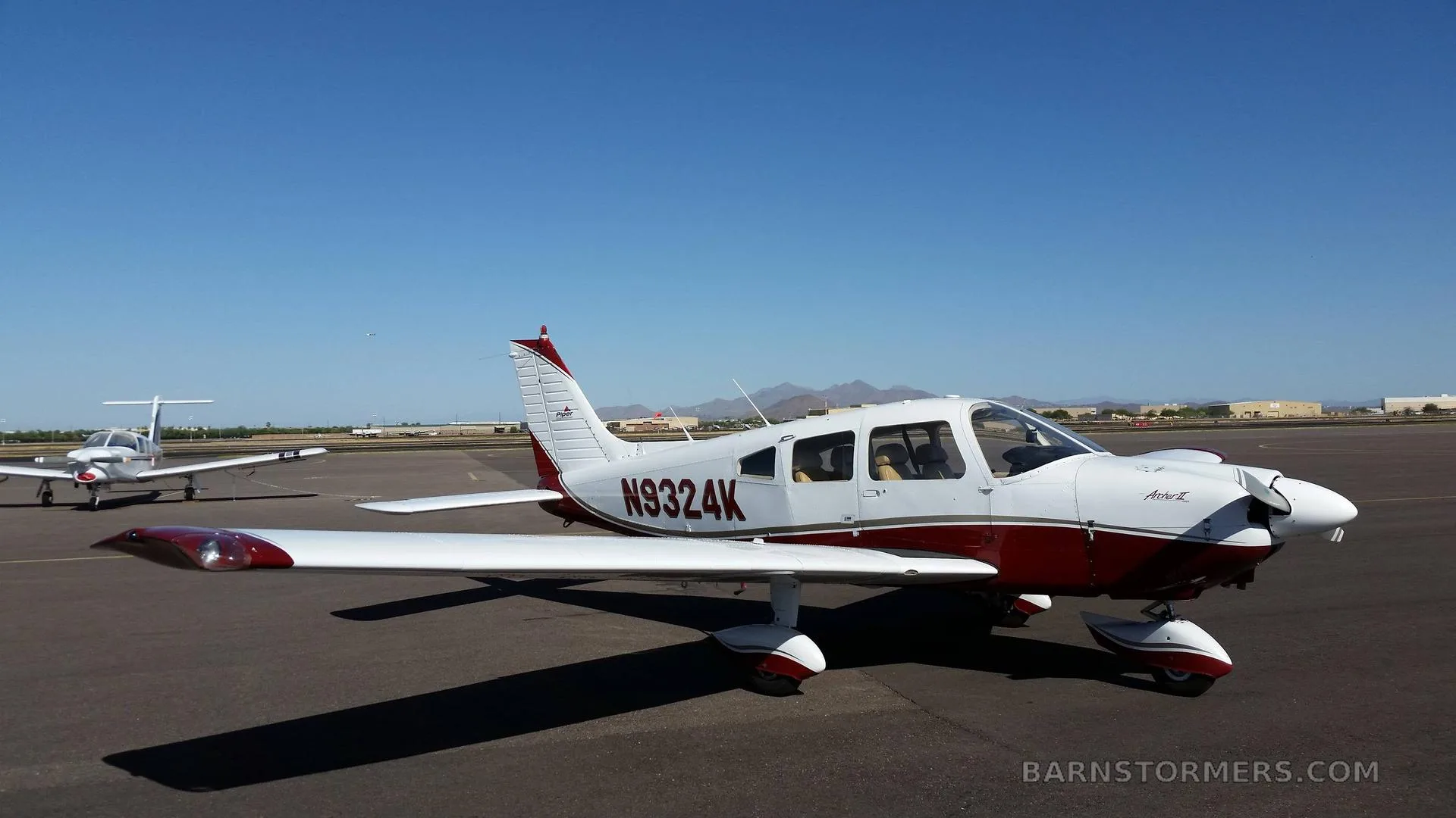 A white and red Piper Archer II (N9324K) parked on an airport tarmac with mountains in the background.