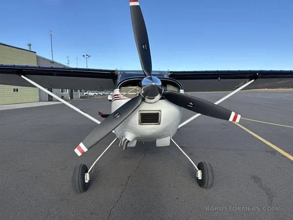 A front view of a white and black single-engine propeller aircraft with a large propeller, parked on an asphalt tarmac.