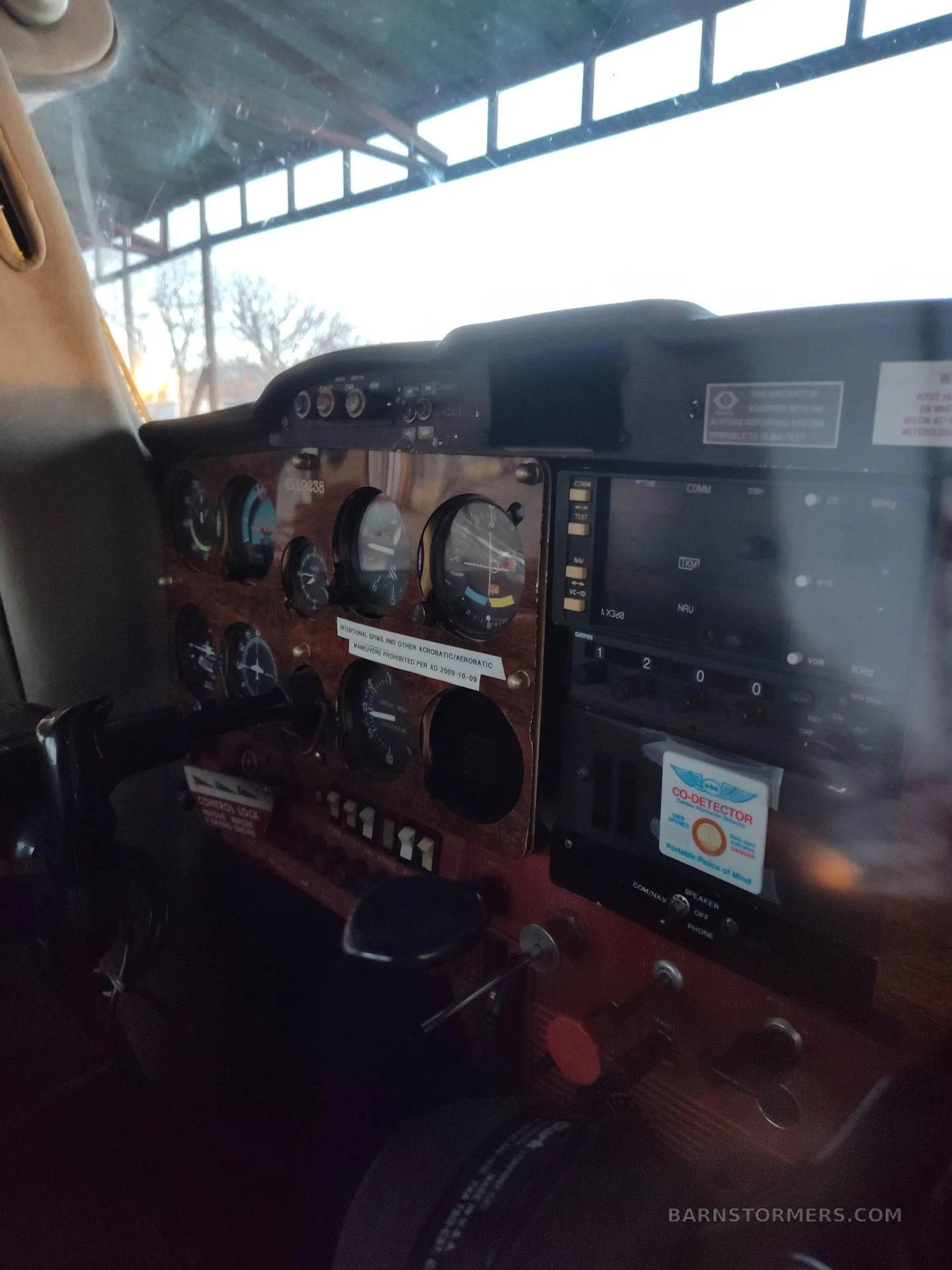 The cockpit instrument panel of a light aircraft, featuring gauges and avionics, with a wooden-look trim.