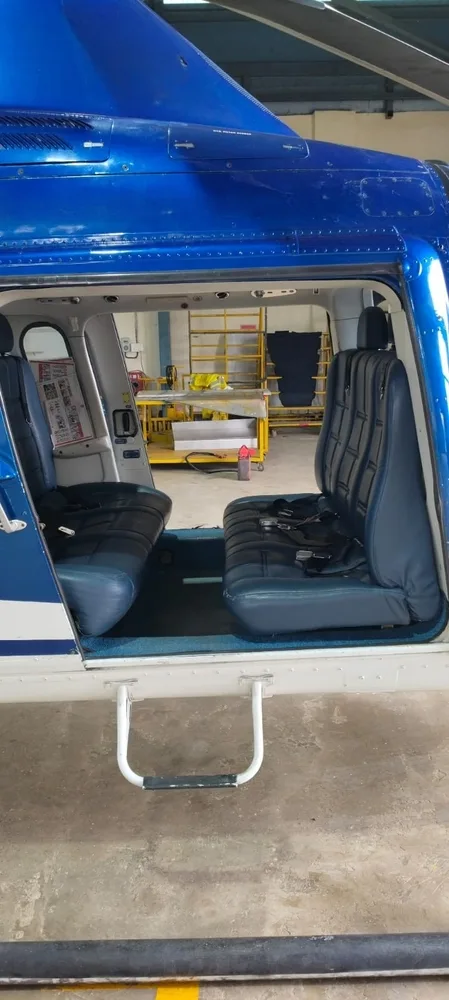 The interior cabin of a helicopter showing two rows of blue quilted seats with seatbelts.