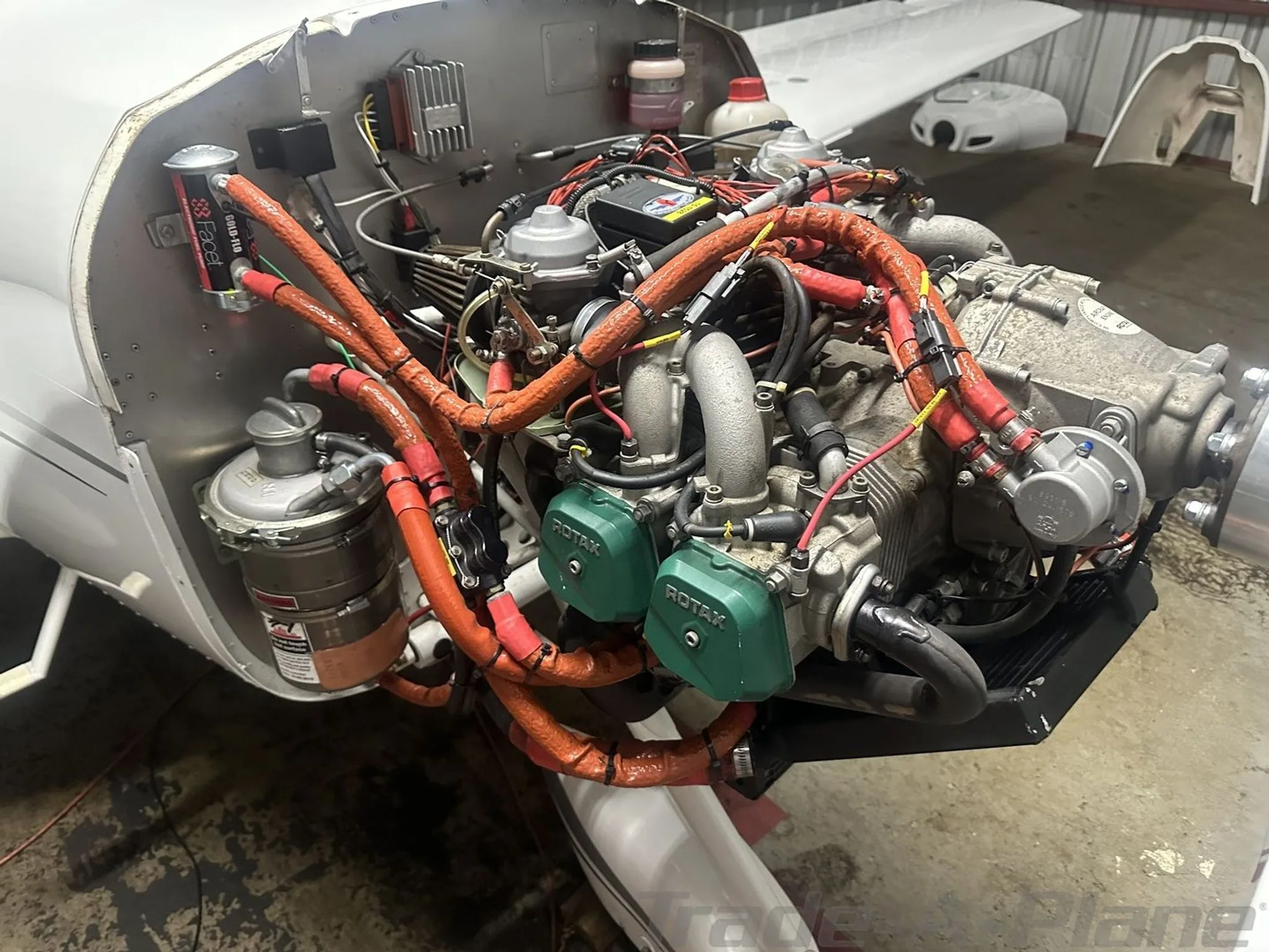 Close-up view of the Rotax aircraft engine with orange-sleeved wiring and hoses.