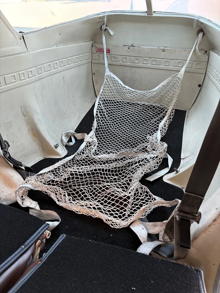 The baggage area with a white cargo net in the rear of a small aircraft cabin.