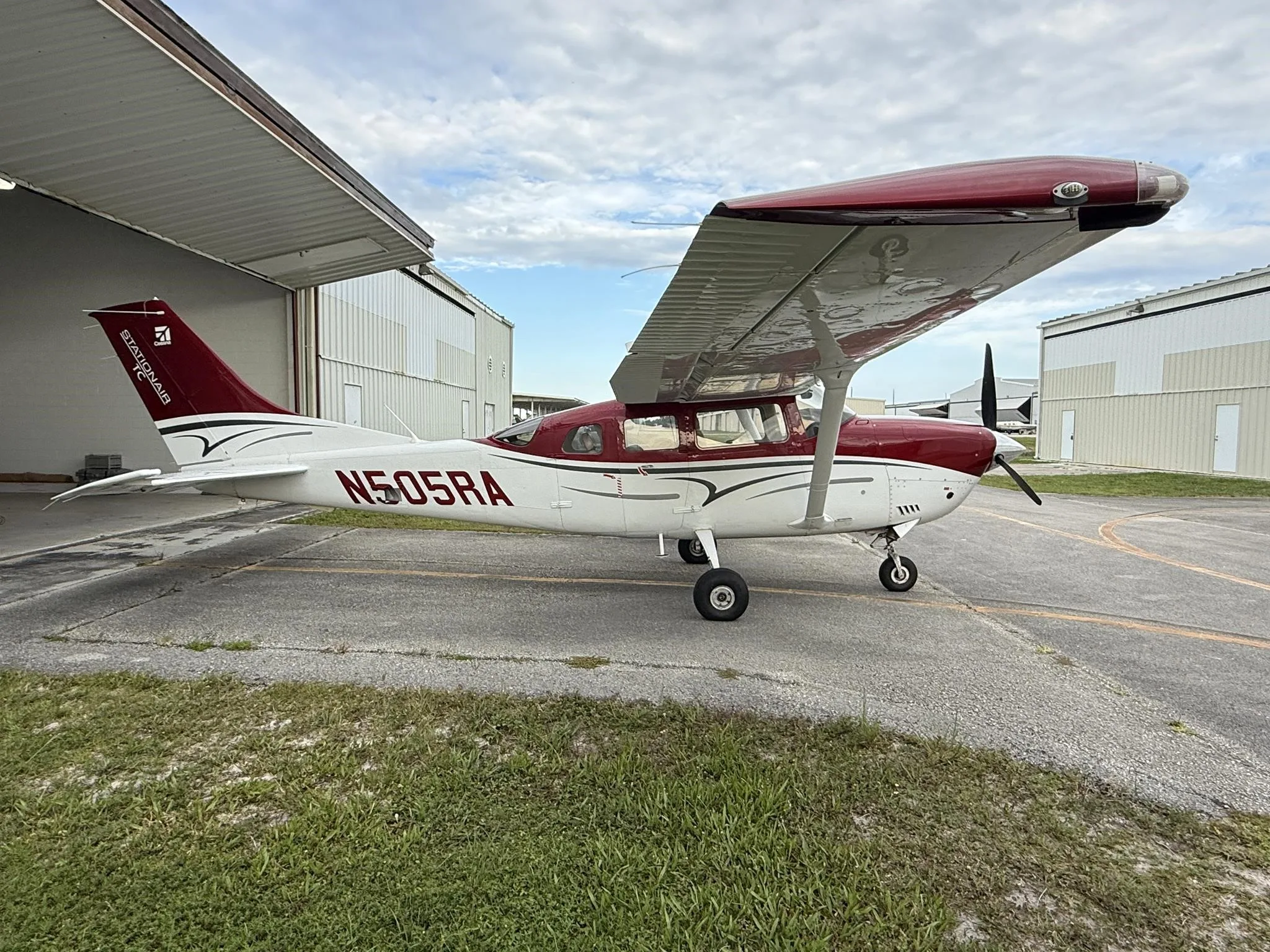 A red and white Cessna Stationair TC aircraft (N505RA) parked partially in a hangar, viewed from the left side.