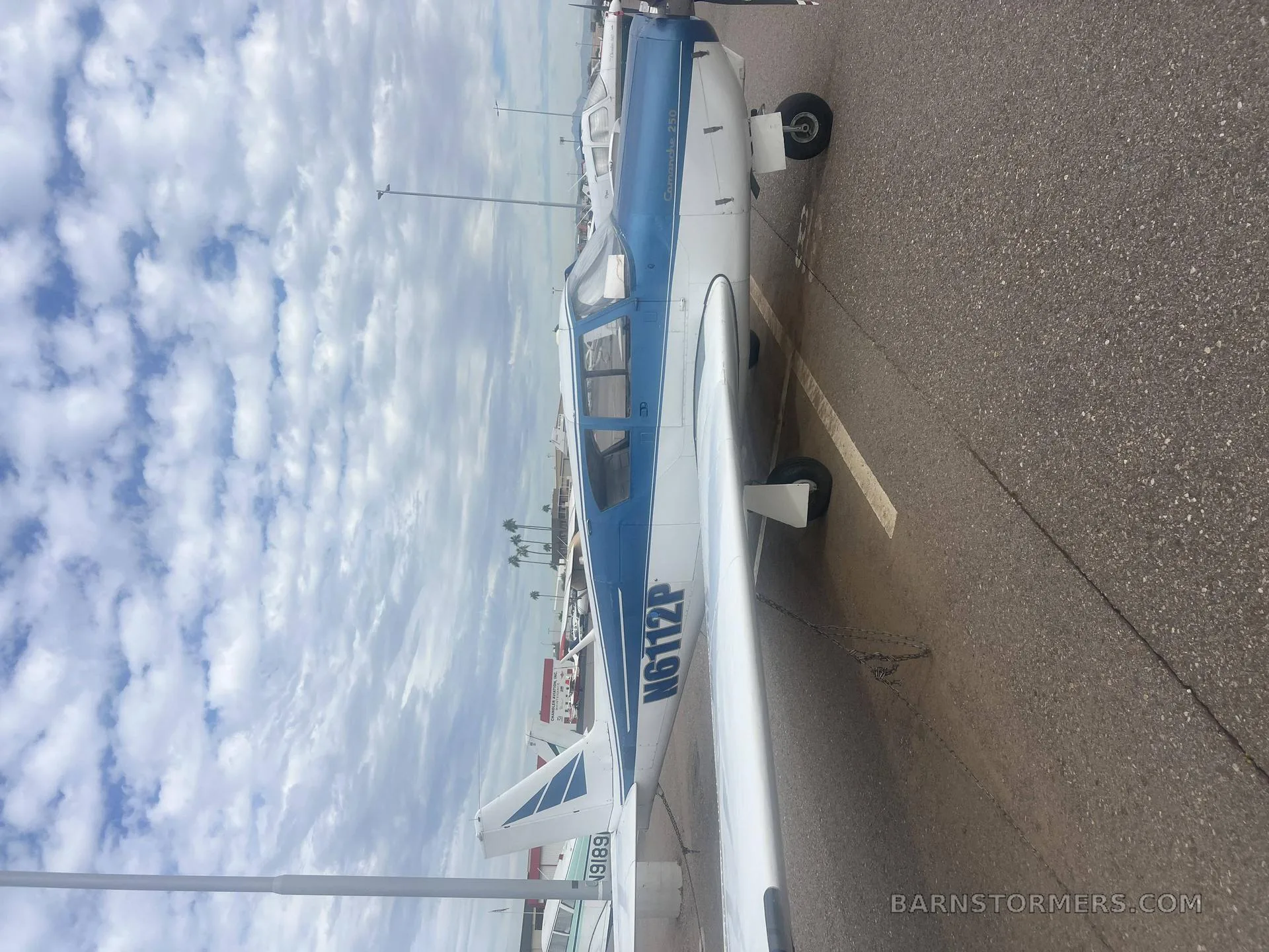 A blue and white single-engine aircraft, tail number N6112P, parked on an asphalt ramp under a cloudy sky.