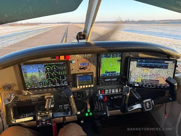 The cockpit of a small aircraft with modern glass panel displays and an iPad mounted, looking out onto a snowy runway.
