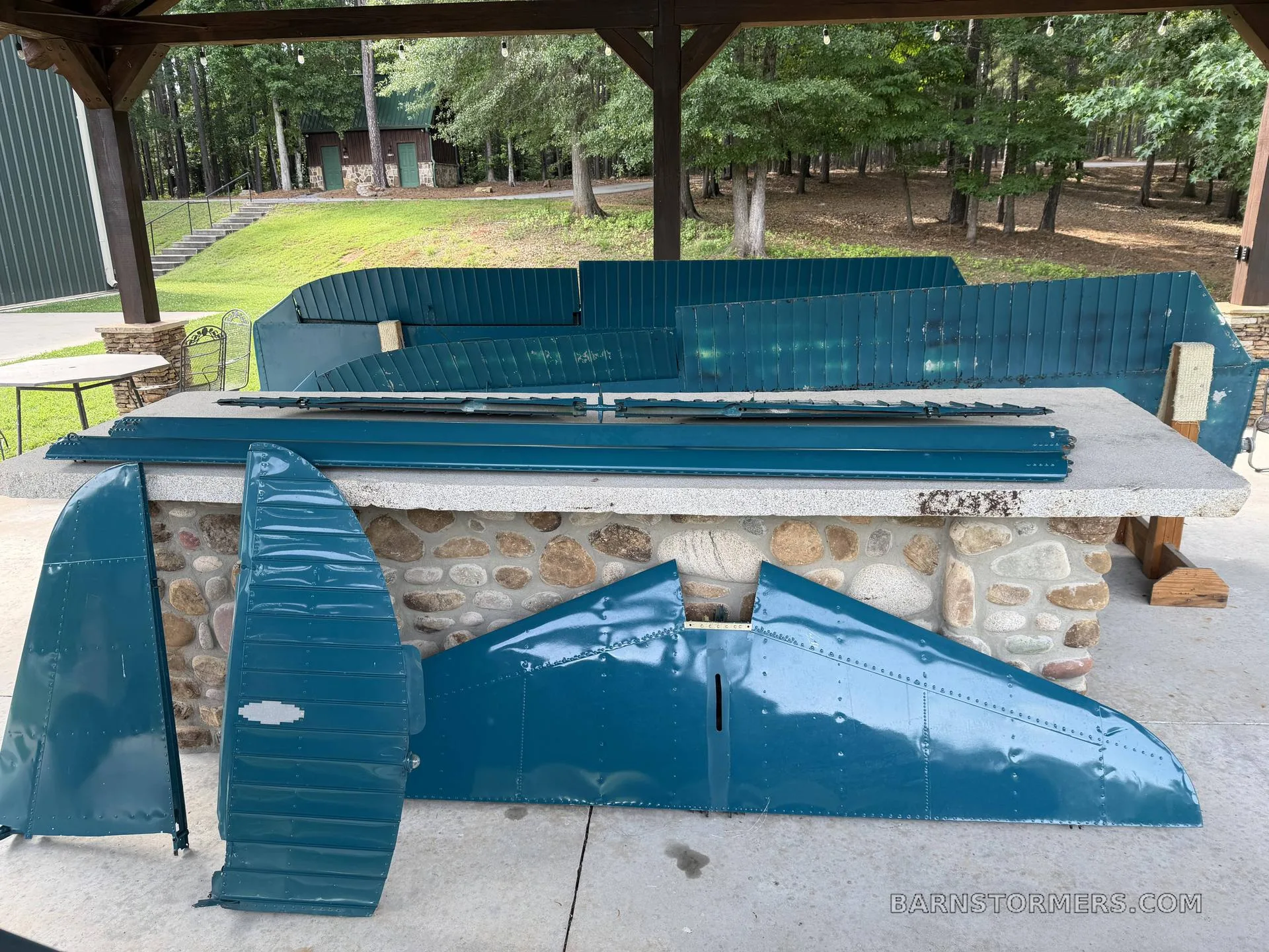 Various teal aircraft wing and tail sections laid out on a stone table and concrete patio.