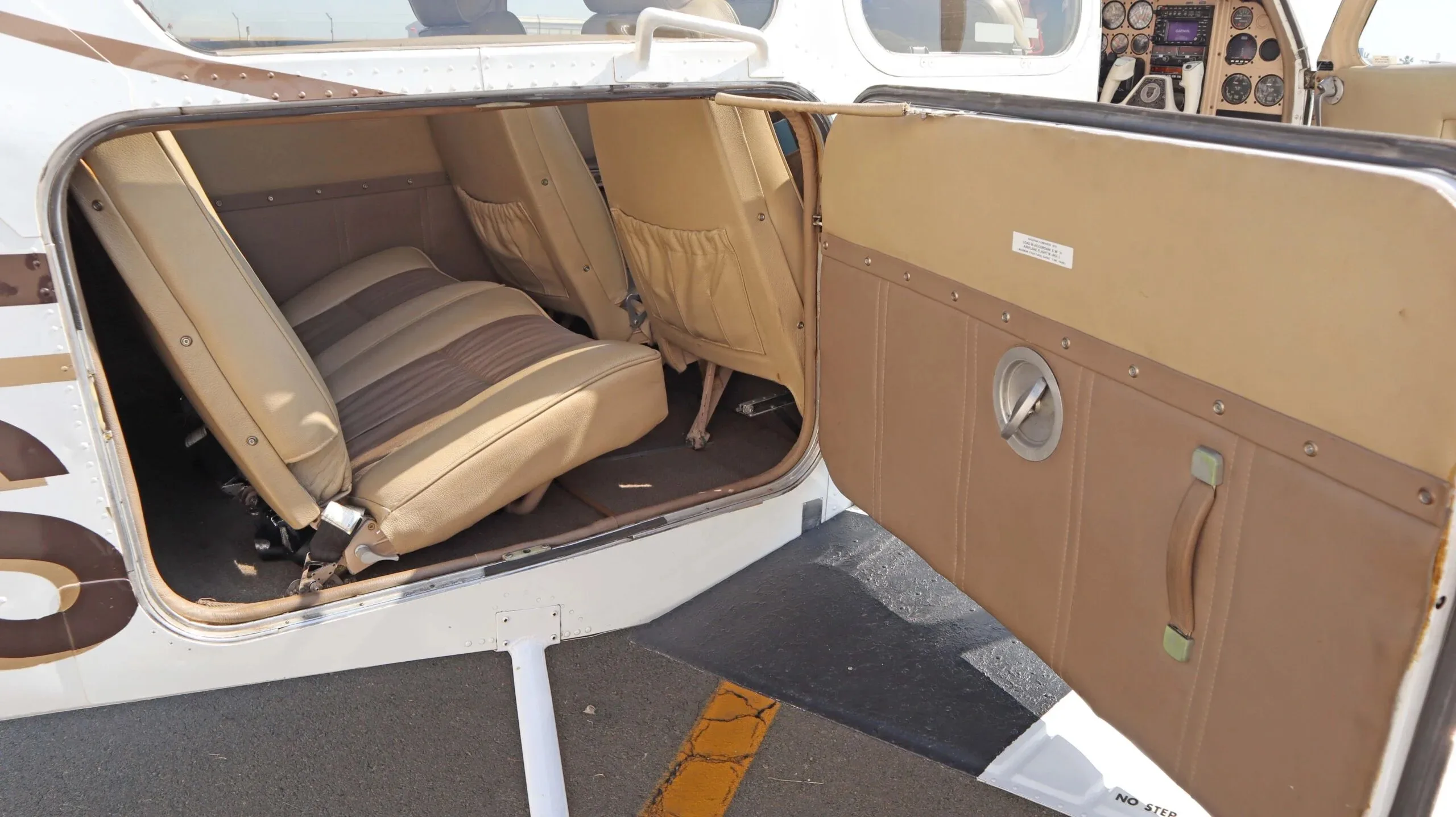 The tan and brown interior cabin of a small aircraft is visible through an open door, showing two rows of seats.