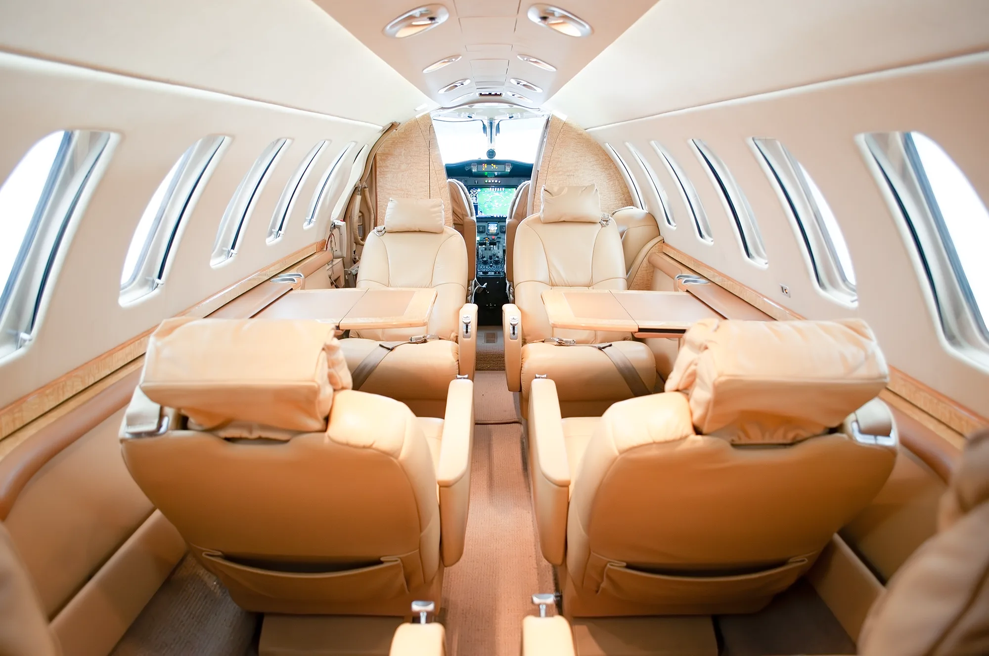 The full view of the tan leather cabin interior of a business jet, looking forward towards the cockpit.