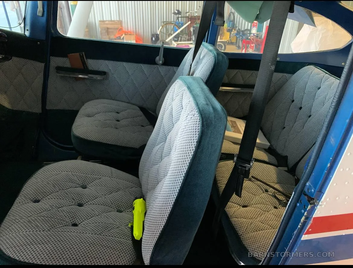 The rear cabin interior of a small aircraft, featuring quilted gray and blue seats with seatbelts.