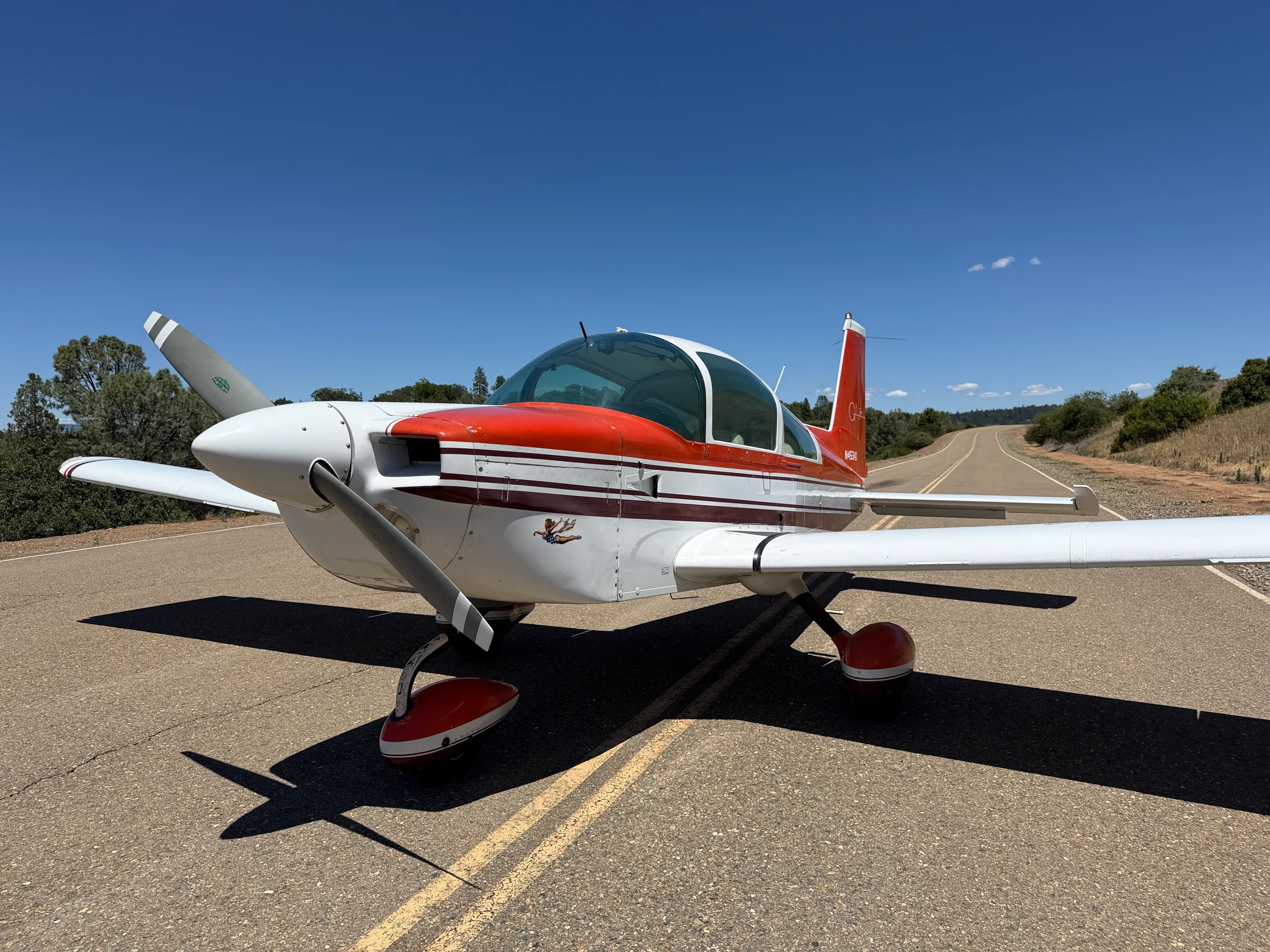A red and white Grumman Tiger aircraft is parked on an asphalt road under a clear blue sky.