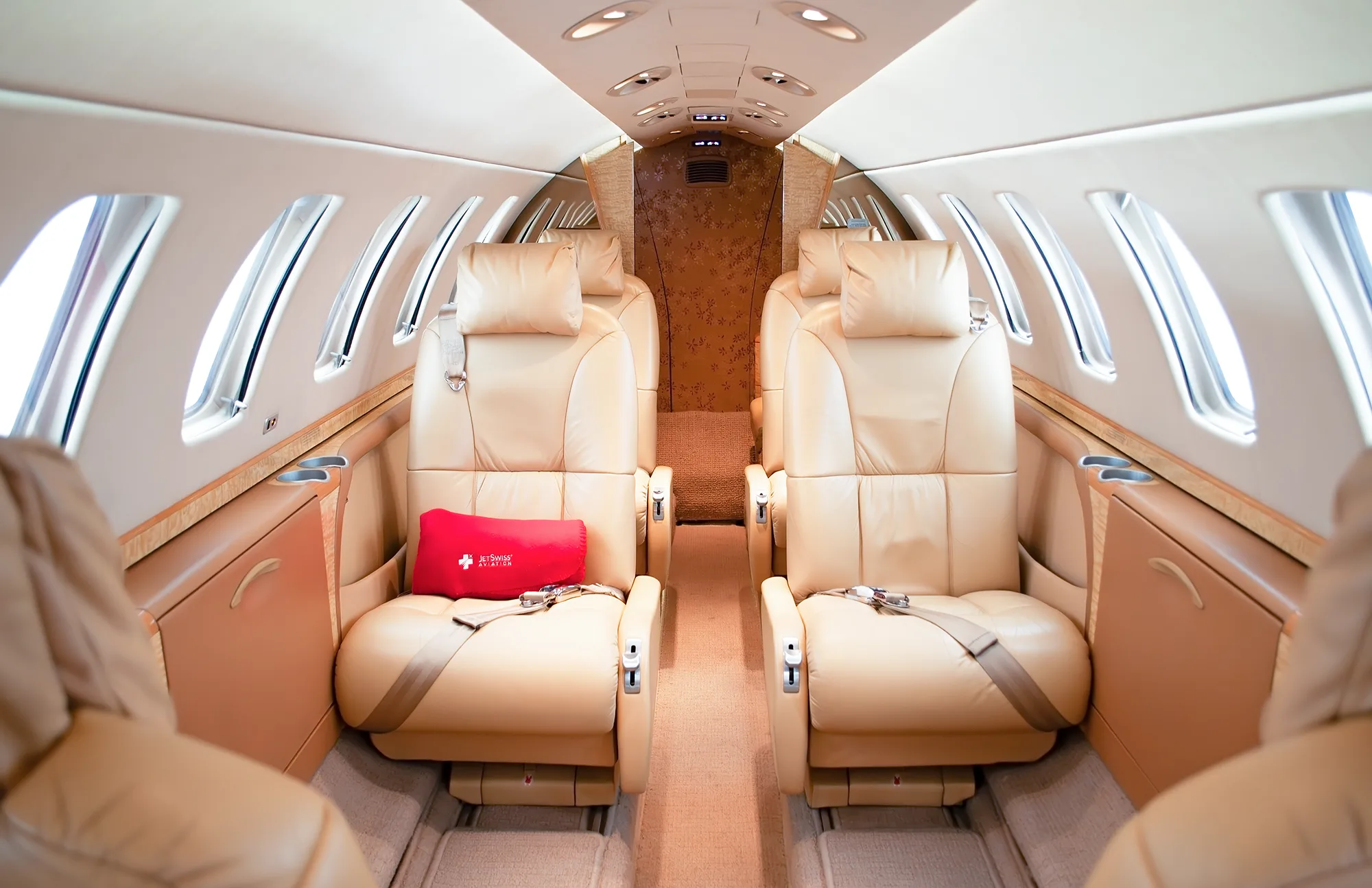 The luxurious tan leather interior cabin of a business jet, showing two rows of seats facing each other.