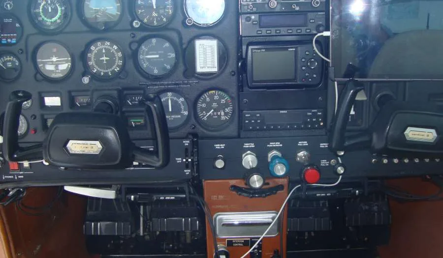 The cockpit instrument panel of a small aircraft, showing gauges, radios, and control yokes.