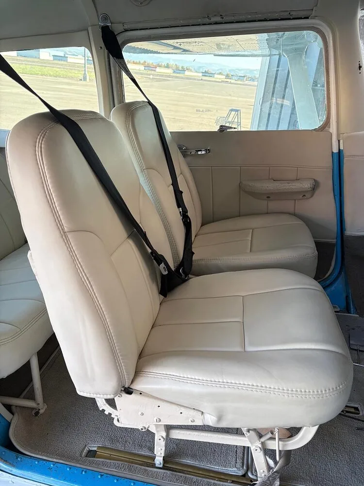 A view of the cream-colored front passenger seats with black seatbelts in the aircraft cabin.