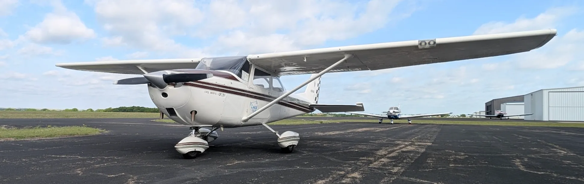 A white Cessna Skyhawk QB, registration N2740L, with a maroon stripe, parked on an airfield tarmac with hangars in the background.