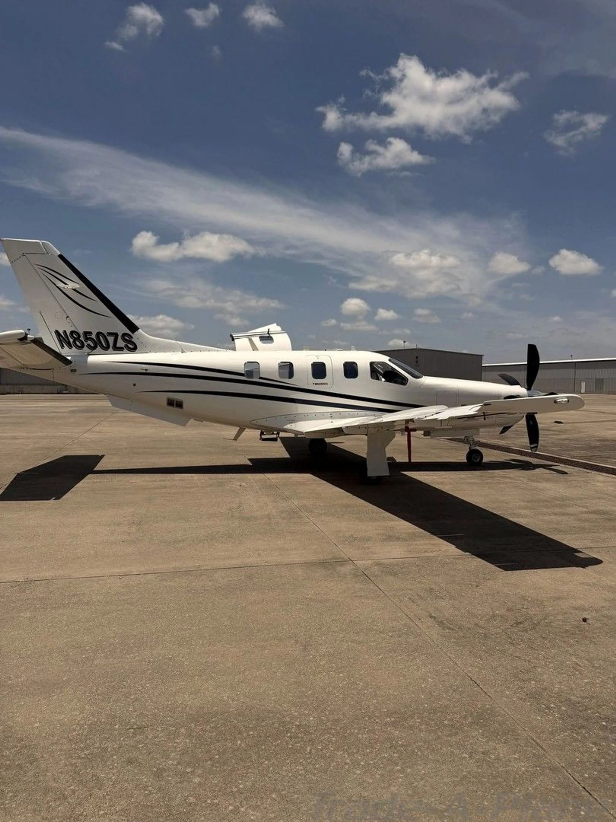 Side view of a white turboprop aircraft with black stripes and registration N850ZS parked on an airfield.