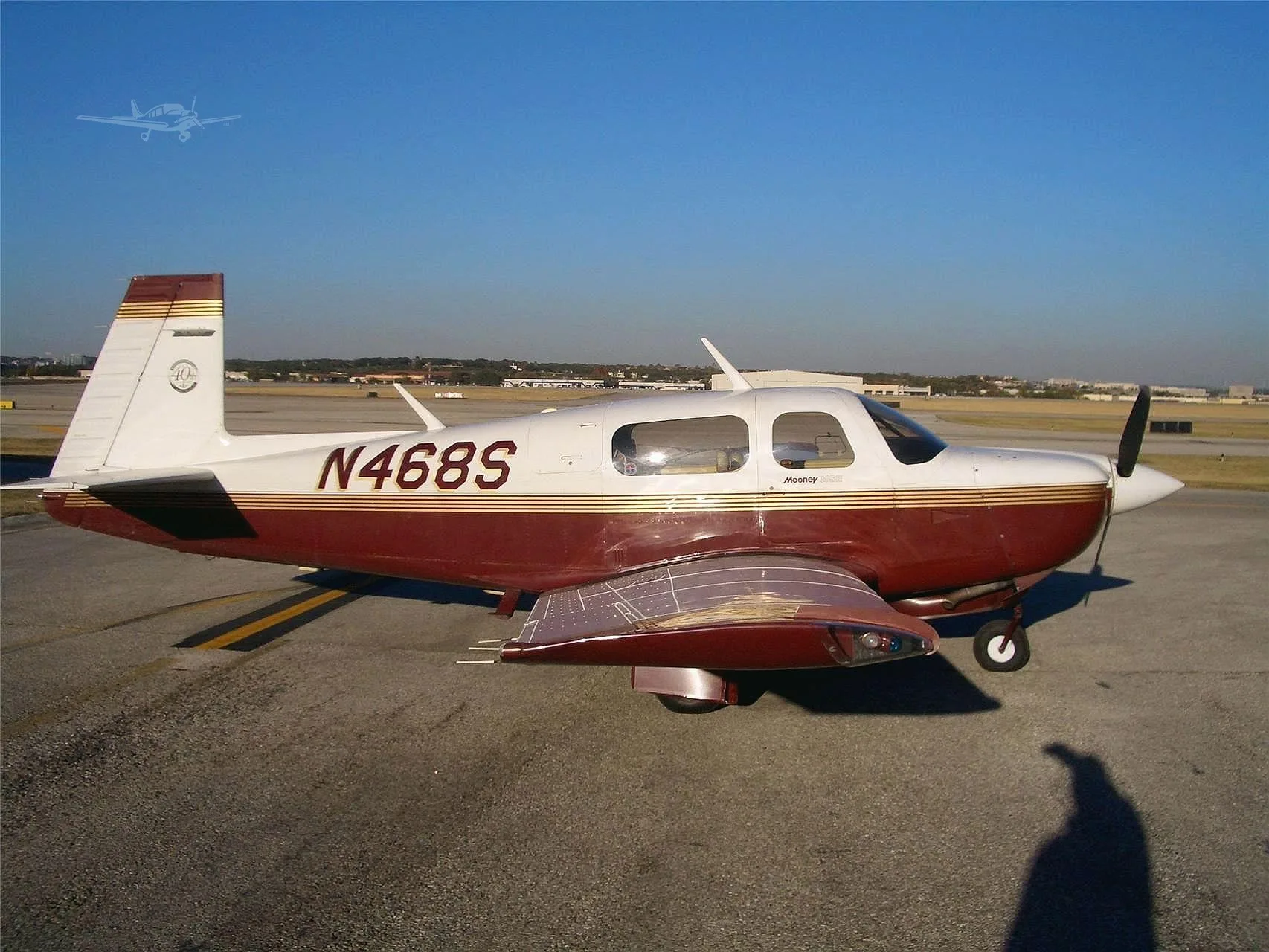 A white and maroon Mooney M20J aircraft, registration N468S, parked on an airport tarmac under a clear blue sky.