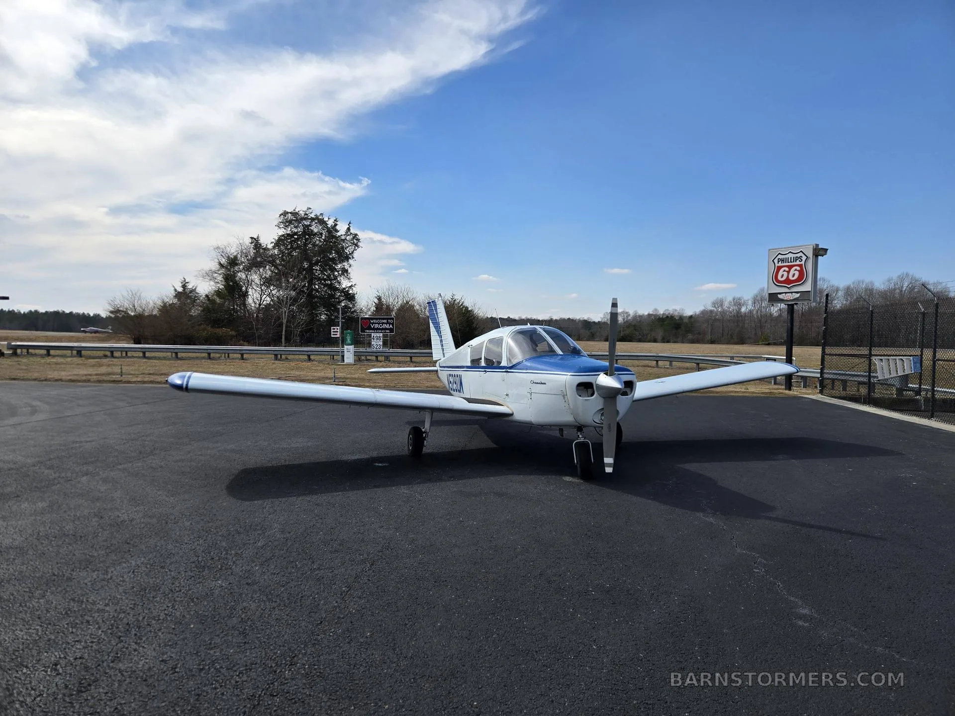 A white and blue single-engine aircraft (N5290W) parked on an asphalt ramp with a Phillips 66 sign.