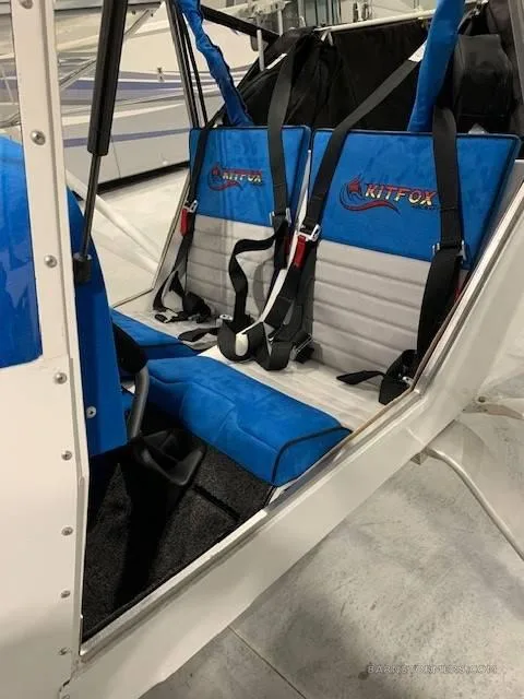 The interior of a Kitfox aircraft, showing two blue and grey seats with "KITFOX" logos and harnesses.