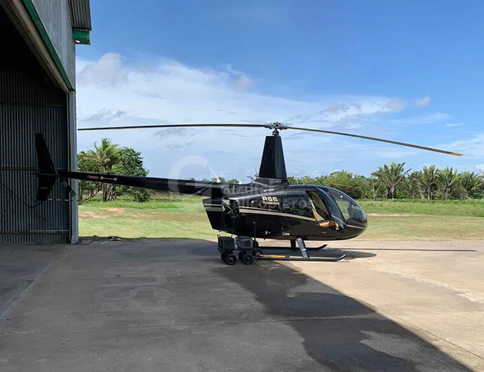 A black Robinson R66 Turbine helicopter with gold accents is parked on a tarmac next to a hangar.