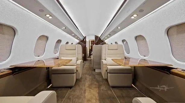 The elegant aircraft cabin features two rows of cream leather seats with fold-out wooden tables and large windows.