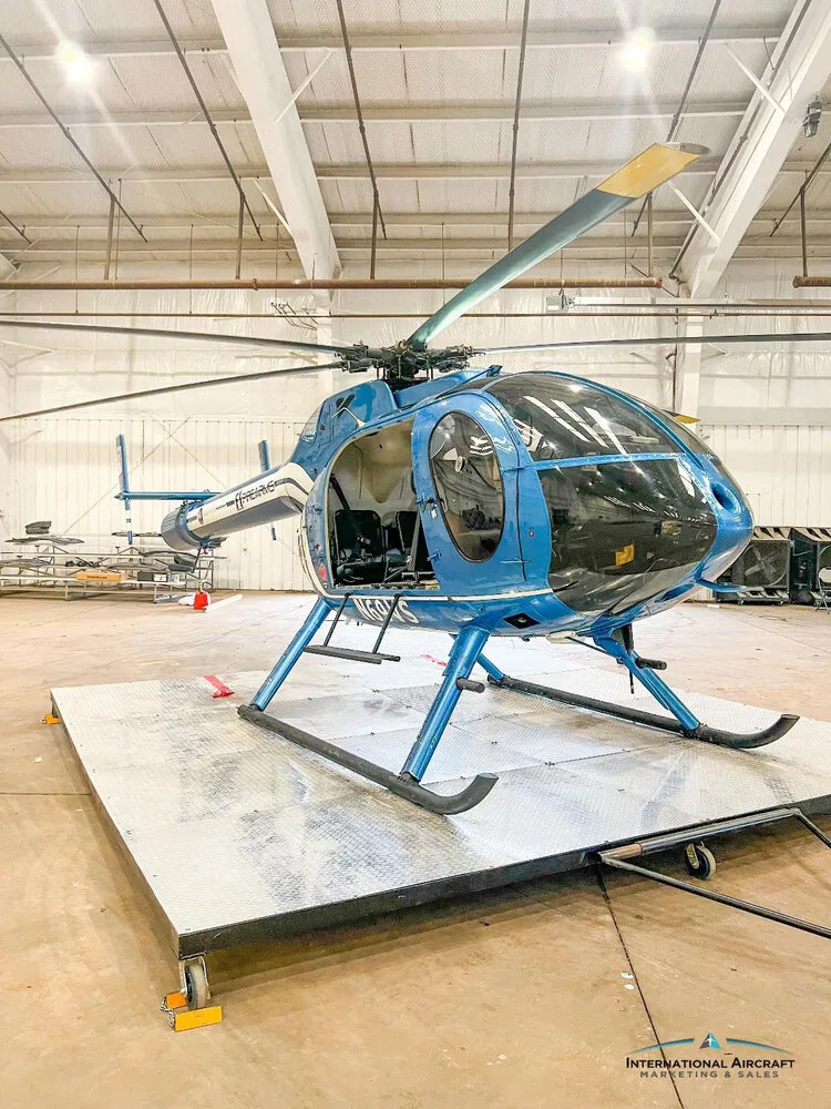 A front-side view of the blue N69VS helicopter with white stripes and F1 FIREARMS branding, parked in a hangar.
