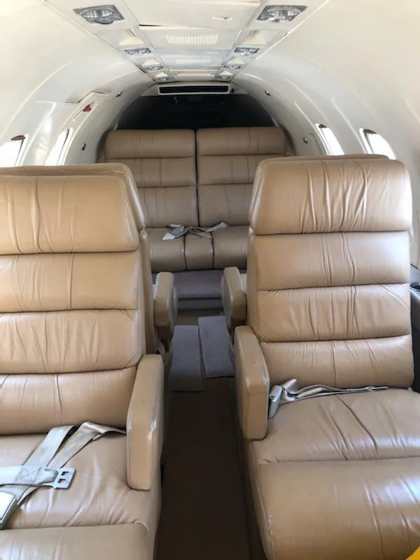 Interior view of an aircraft cabin showing multiple tan leather seats arranged in a club configuration.
