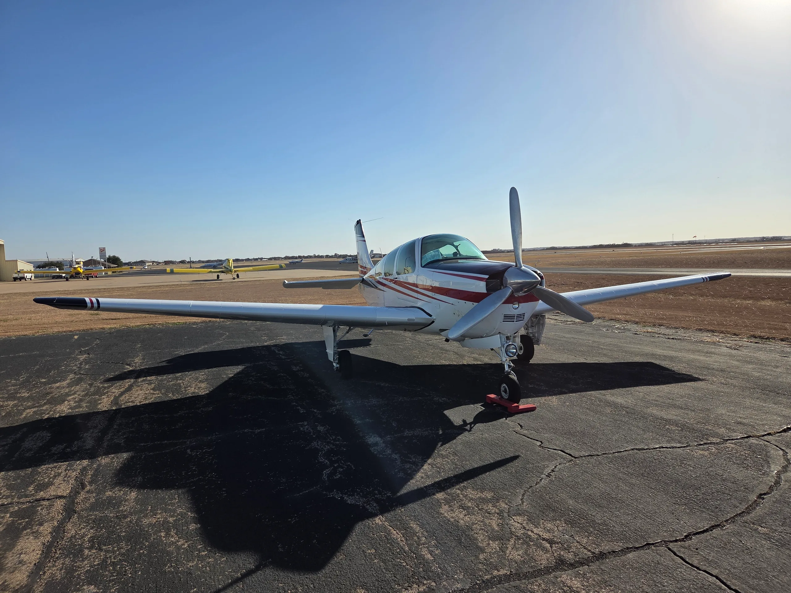 A white and red single-engine aircraft with a propeller on an asphalt ramp under a clear sky.