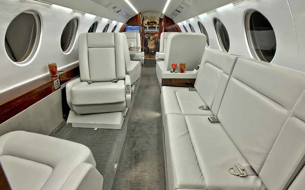 The luxurious cabin interior of a business jet with light gray leather seats and dark wood paneling.
