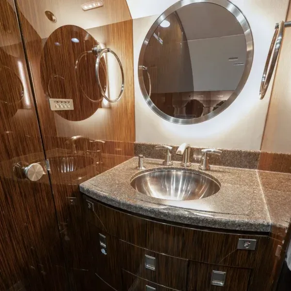 A private jet lavatory with a modern sink, granite countertop, and dark wood paneling.