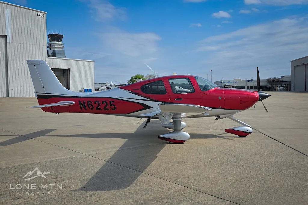 A red and silver Cirrus SR22 aircraft, N6225, parked on an airport apron with a control tower in the background.