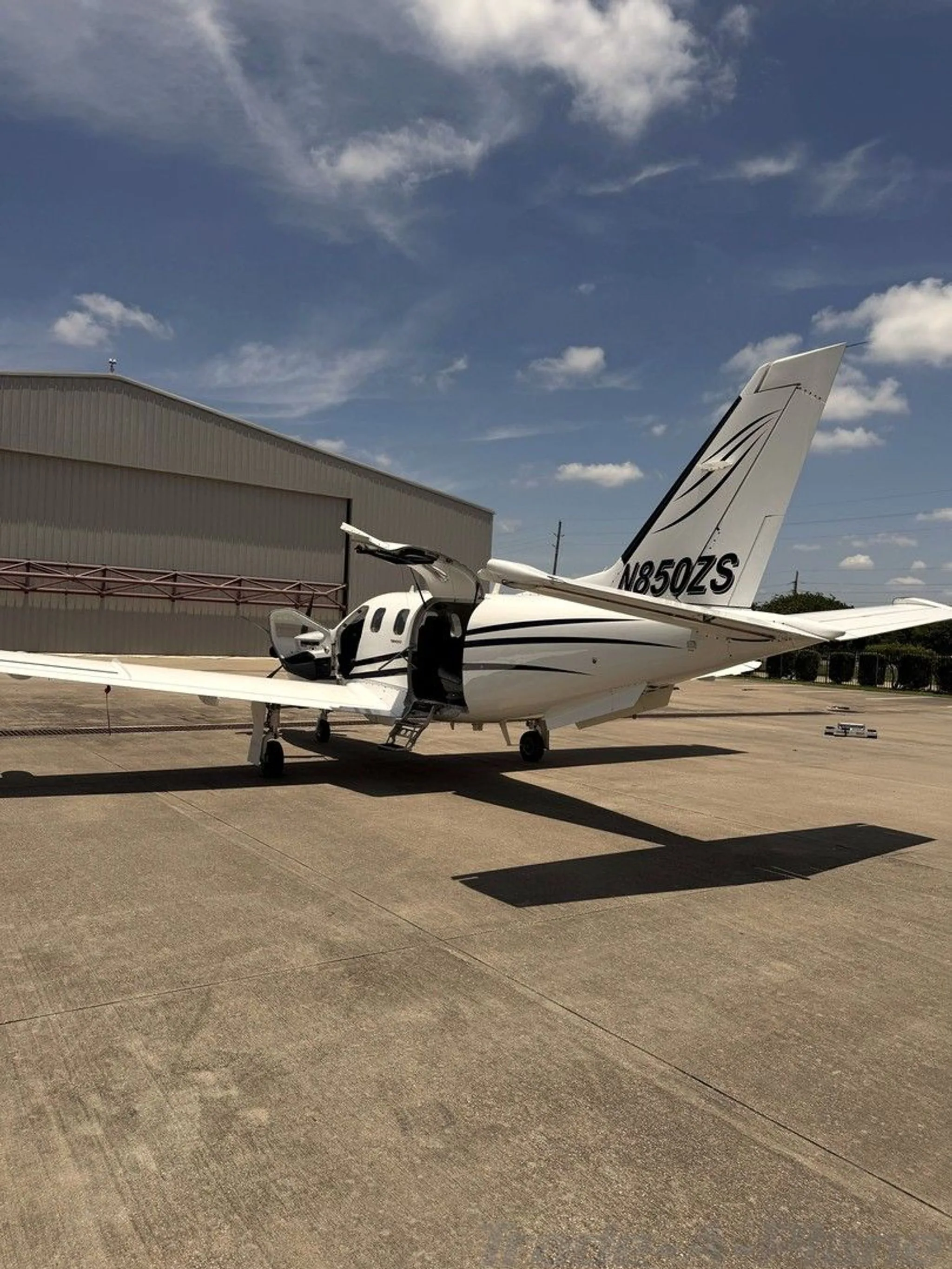 Rear-side view of a white turboprop aircraft with black stripes and registration N850ZS, showing open cabin doors.