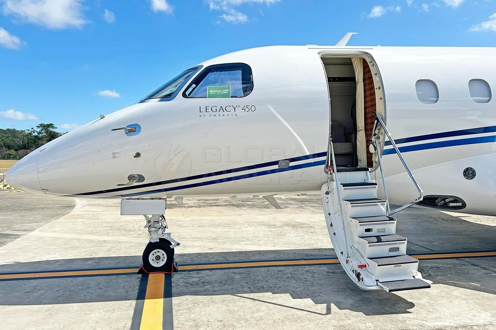 Close-up of the nose and open passenger door with stairs of a white Embraer Legacy 450 business jet.