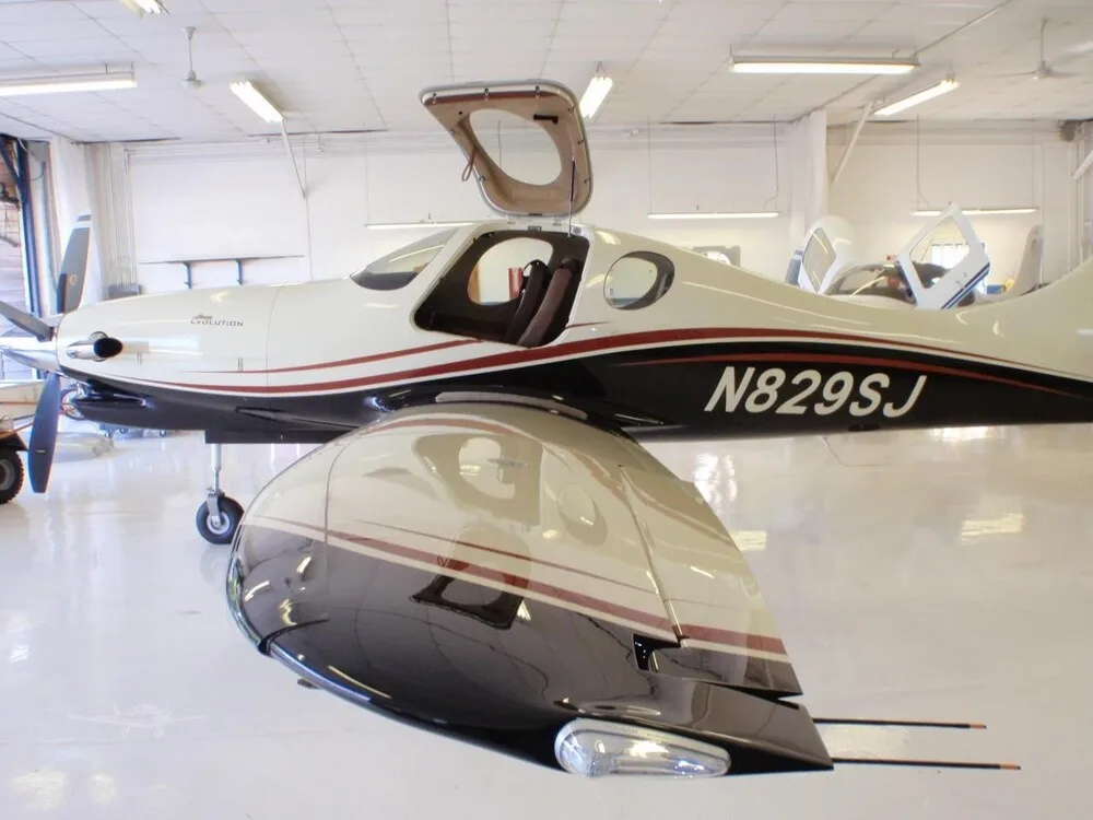 A white and black Lancair Evolution aircraft with red stripes, showing the N829SJ registration and open doors, in a hangar.