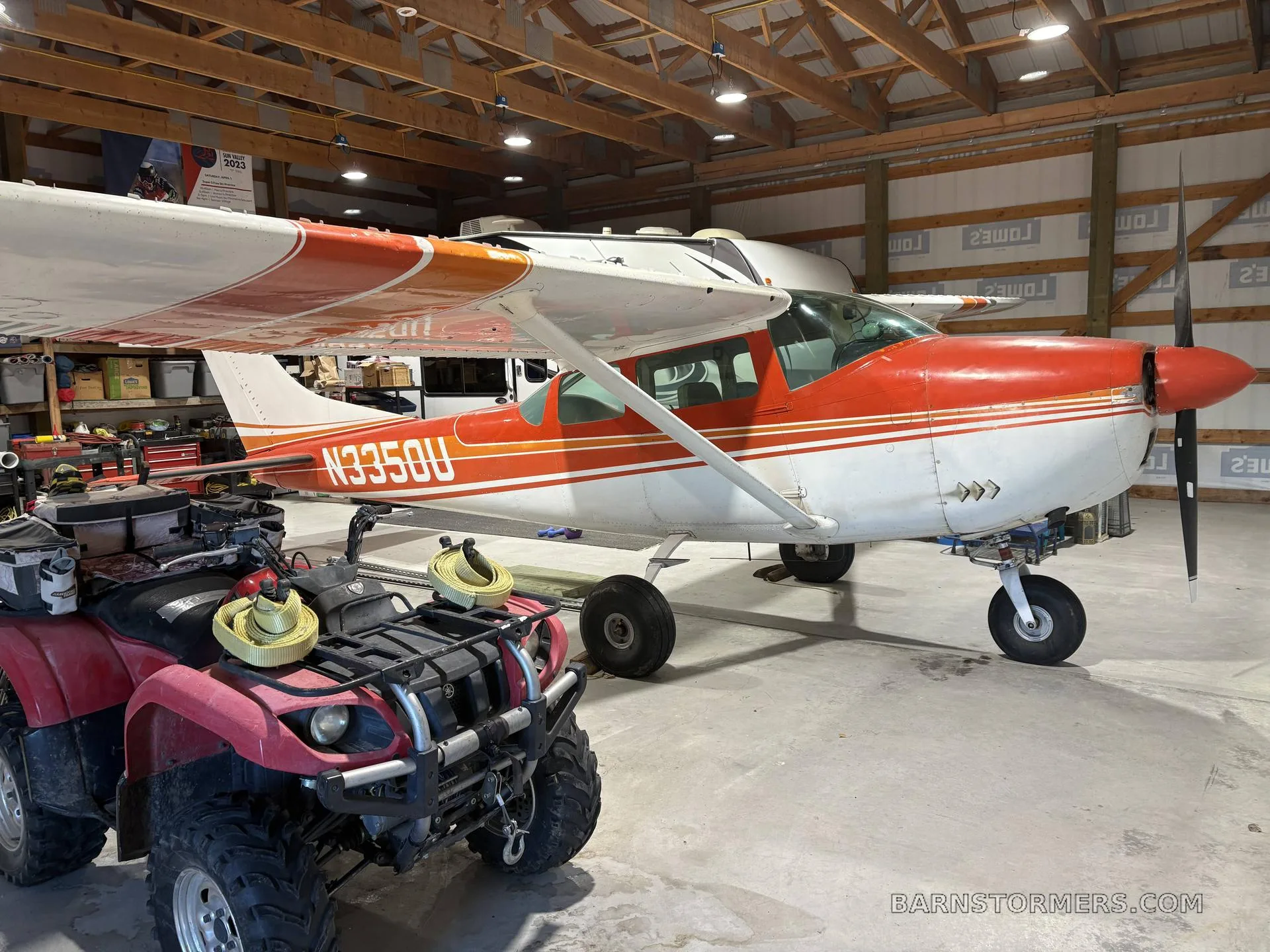A red and white Cessna 182 Skylane (N3350U) is parked inside a hangar next to a red ATV.