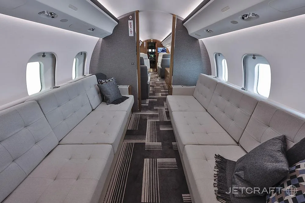 The aft section of the aircraft cabin with two long grey upholstered divans facing each other.