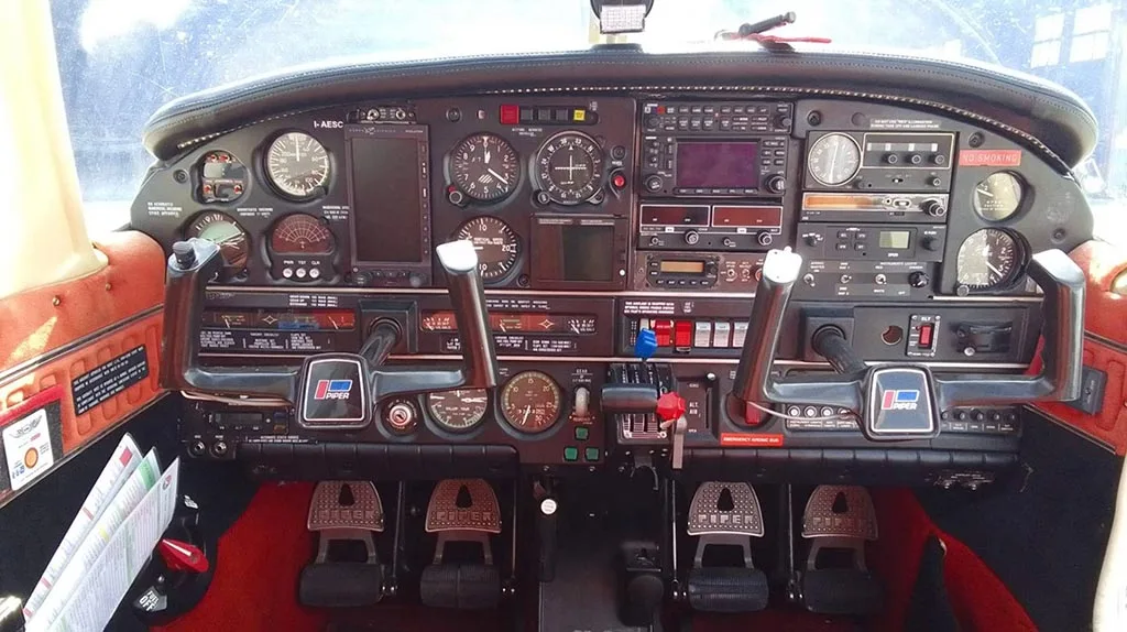 The detailed instrument panel and dual yokes of a Piper PA-28 aircraft cockpit.