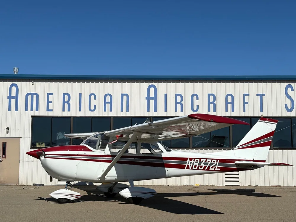 A white and red Cessna 172 Skyhawk aircraft (N8372L) parked on an airfield in front of a hangar.