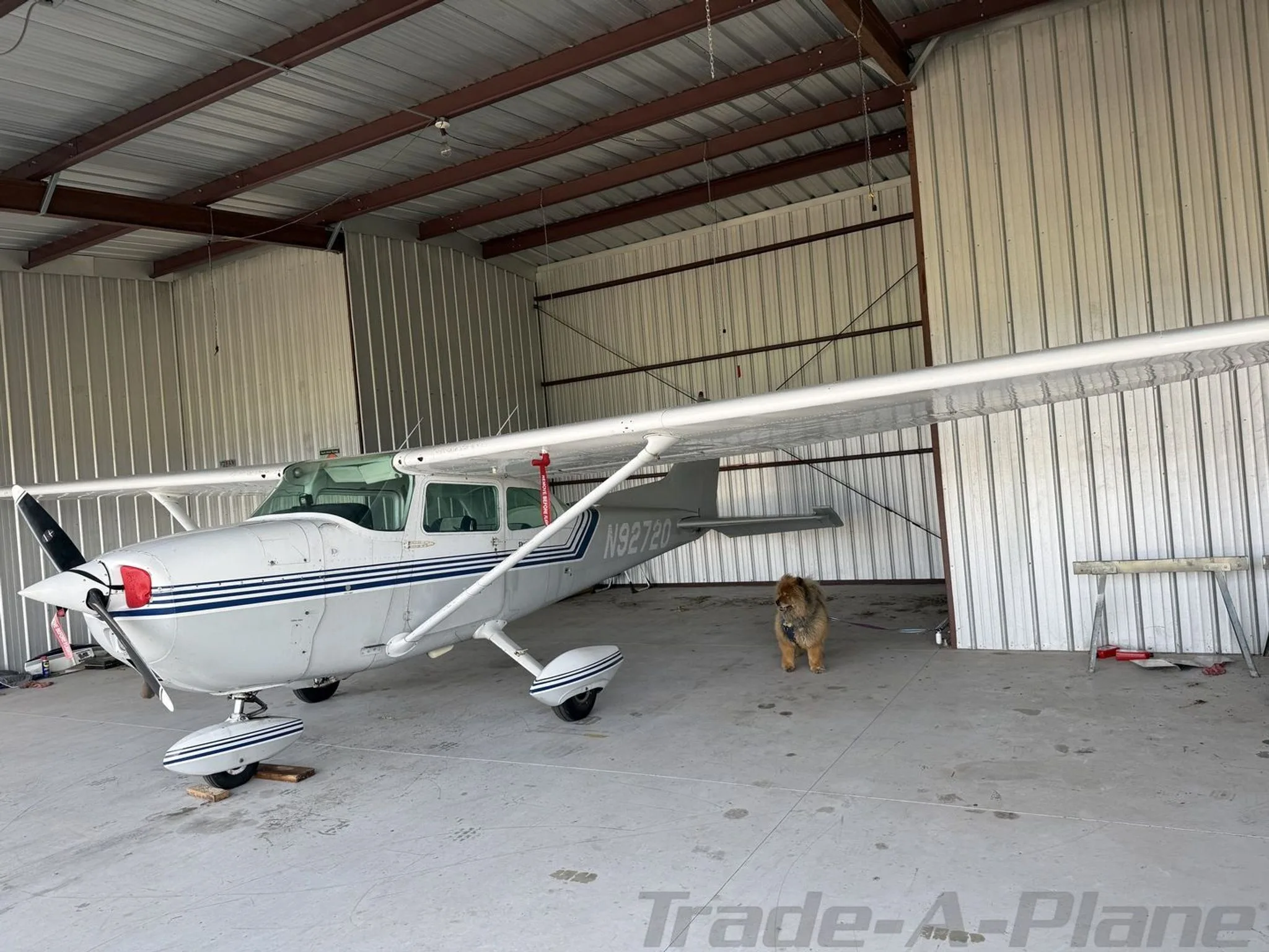A white Cessna Skyhawk with blue stripes and tail number N92720 parked inside a hangar, viewed from the front-right.