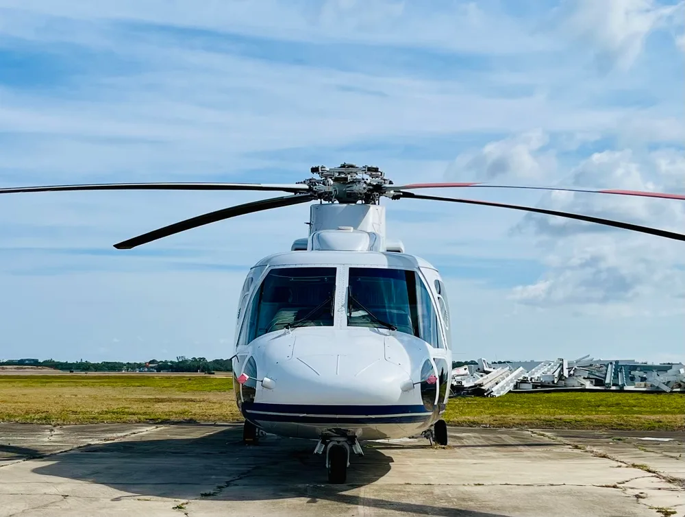 Front view of a white and blue helicopter with its main rotor blades extended, parked on an airfield.