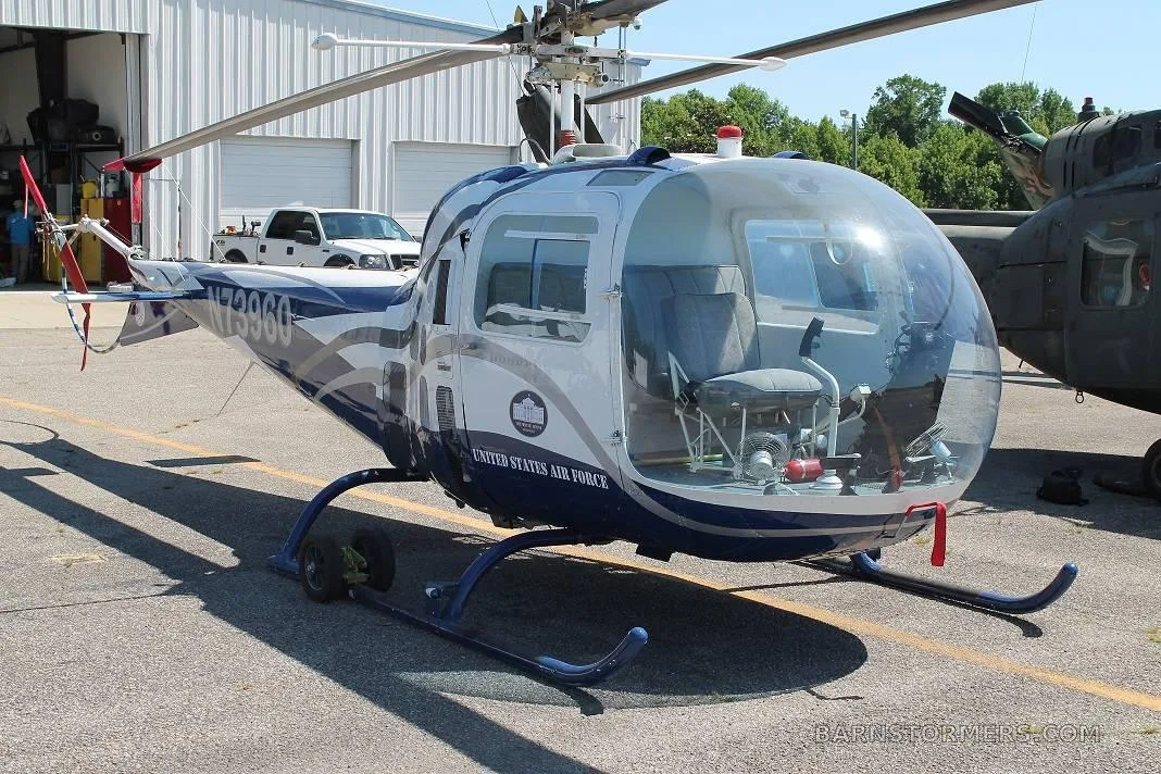 A white and blue helicopter with 'UNITED STATES AIR FORCE' text and registration N73960, parked on asphalt with a white truck and hangar in the background.