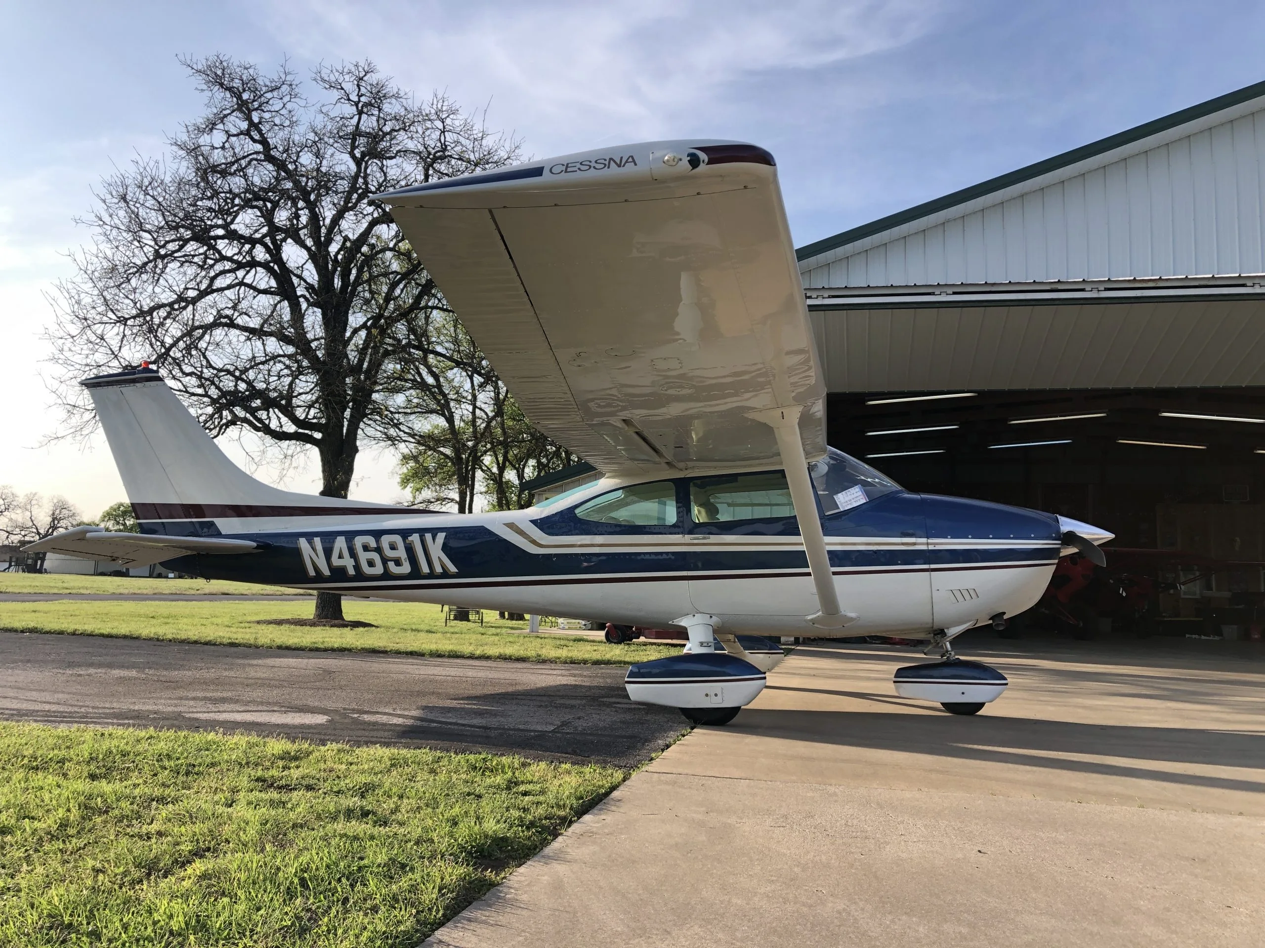 A blue and white Cessna aircraft with registration N4691K parked on an asphalt ramp in front of an open hangar.