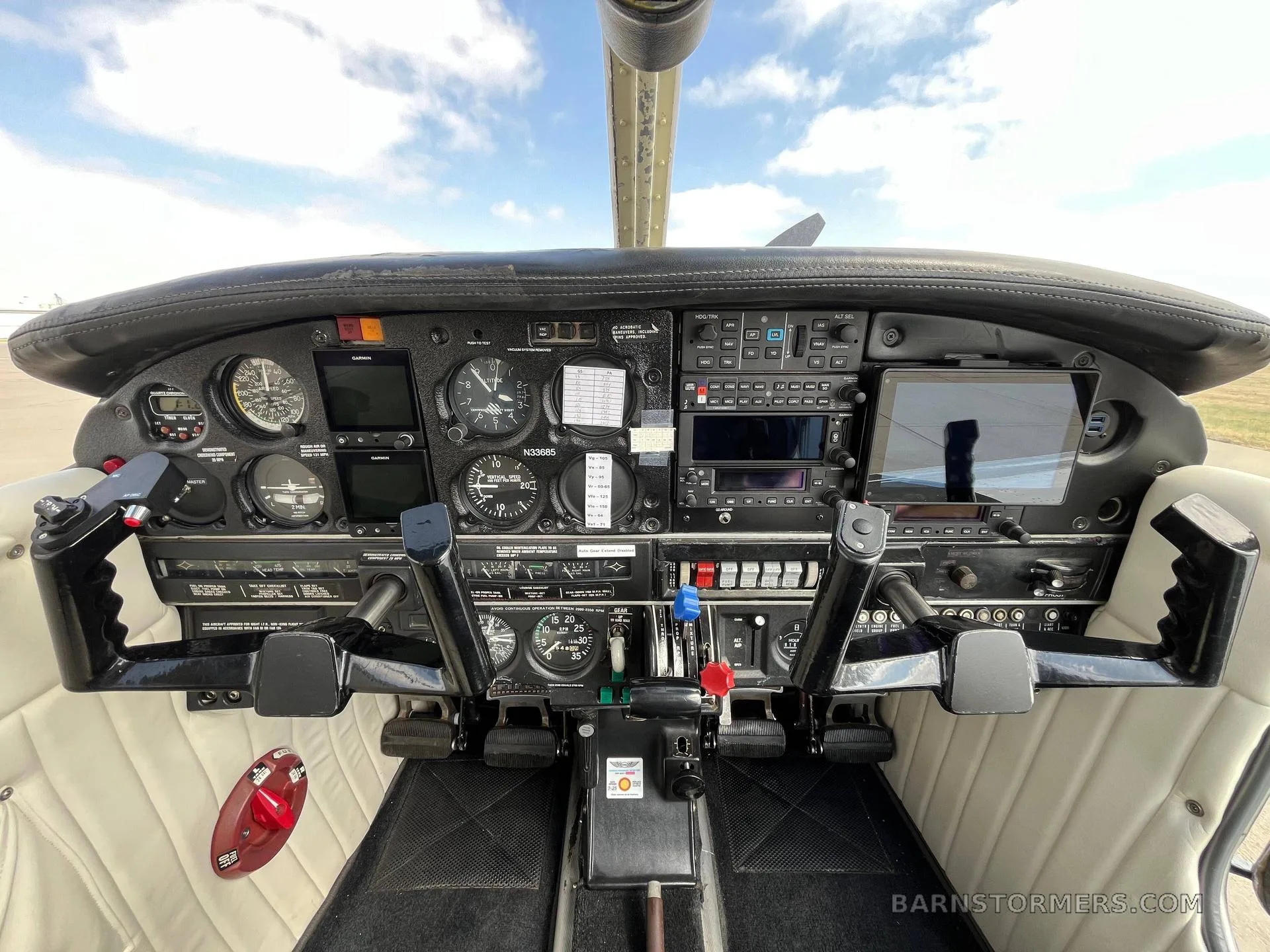 The cockpit of a light aircraft, showing the instrument panel with analog gauges and modern digital displays, and two control yokes.