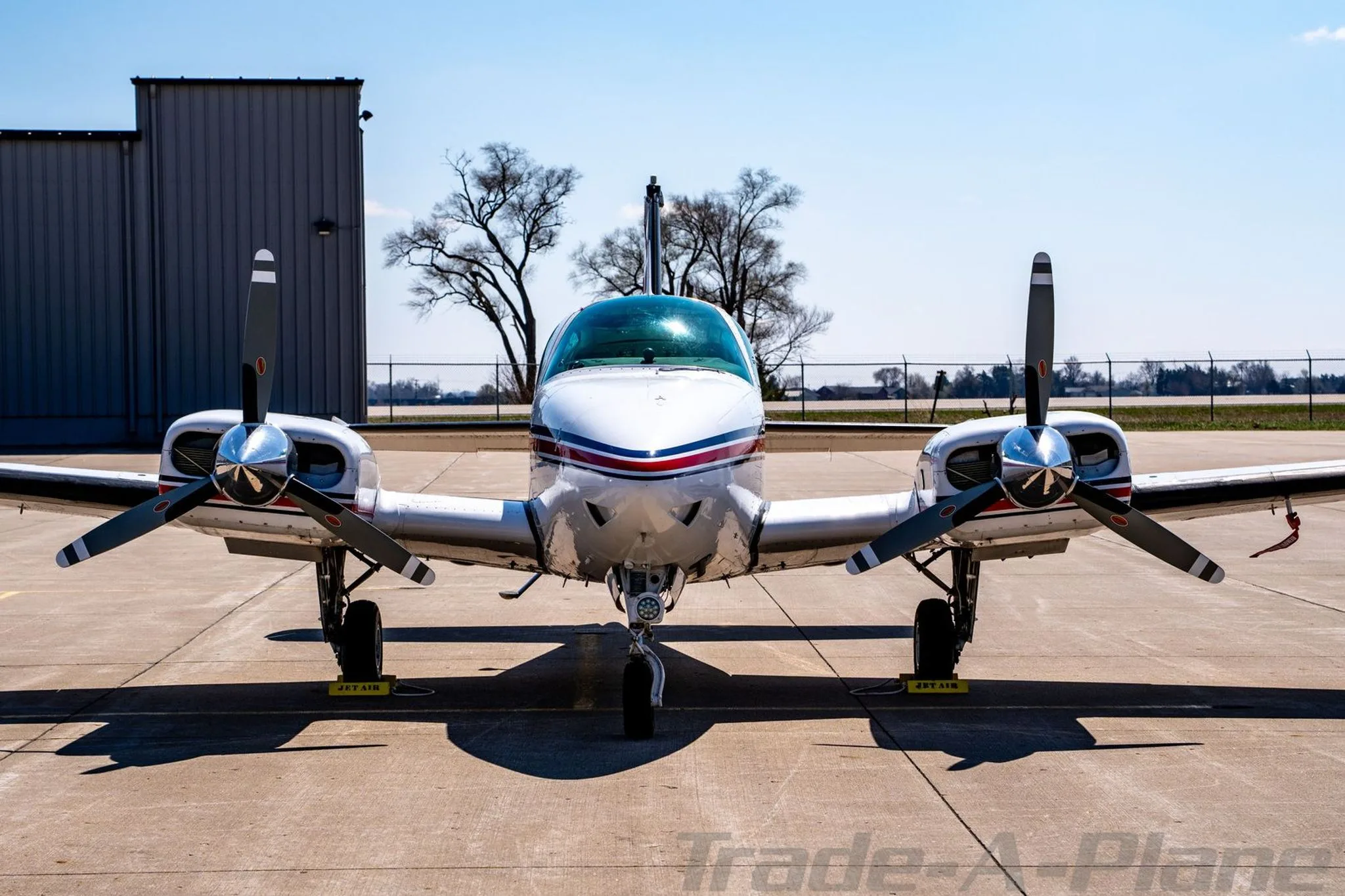 Head-on view of the N4UF twin-engine Beechcraft Baron with red and blue stripes on an airfield.