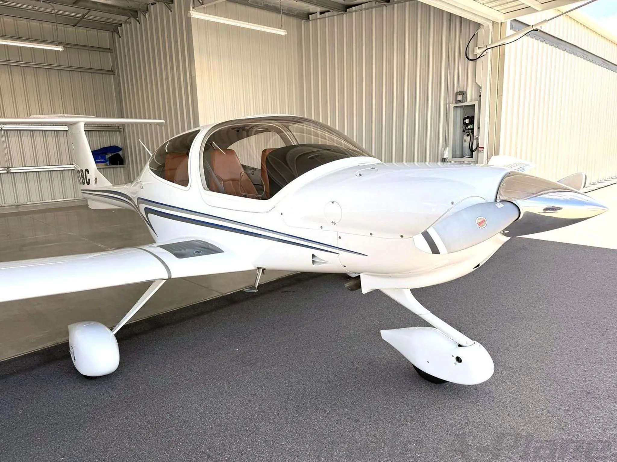 A front-quarter view of a white Diamond Star DA40 XLS aircraft with blue and grey stripes, tail number N853BC, parked in a hangar.