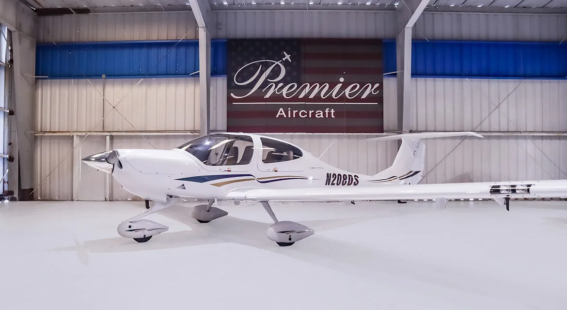 A white Diamond DA40 Star aircraft with gold and purple stripes, registration N208DS, parked in a hangar.